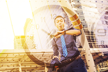 Double Exposure of Confident young man, holding suit with Briefcase, looking at his watch while standing outdoors with Clock , In time appointment Concept.の写真素材