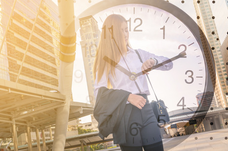 Double Exposure of Business Woman Looking at Watch in Modern City and Clock as Time management conceptの写真素材