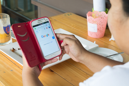 Nakhon Ratchasima, Thailand, May 26, 2017: Woman searching Digital information on something with Her Mobile phone and Google website, the most popular search engine in the world, in Restaurant while she have lunch.のeditorial素材