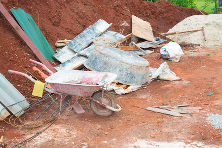 Grunge Red Wheelbarrow with Construction Tools and Material with Background of Soil and steel barの写真素材