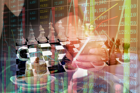 Double Exposure of Businessman use Digital Wireless Smartphone or Mobilephone with Chess and Financial Stock market Graph or Chart as Business Technology Equipment and Leadership Innovation Concept.の写真素材