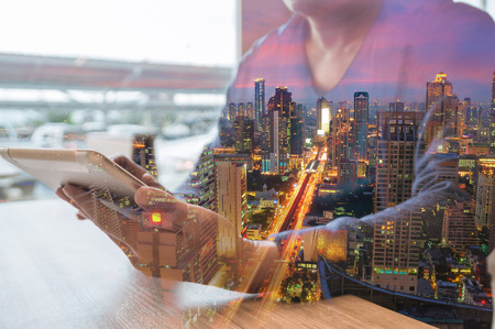 Double Exposure Of Man or Male use Digital Tablet Wireless thinking with Office building Glow at Night as Business Teamwork or Human Resources Strategy Concept.の写真素材