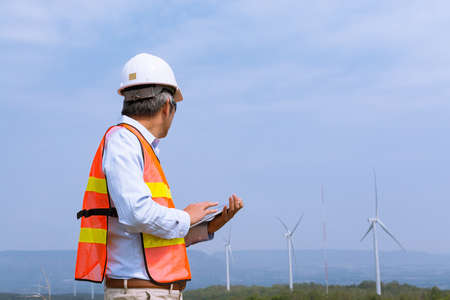 Male Architect Engineer or Businessman wear Hardhat survey Wind Turbine Power Generator Field Site Project with Smart Tablet Device as Ecology or Power Alternative Innovation Technologyの写真素材