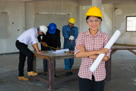Woman as Foreman wear Yellow Hardhat holding Blueprint Standing with construction Team worker or Colleague as Teamwork Partnership and Business collaboration Concept.の写真素材
