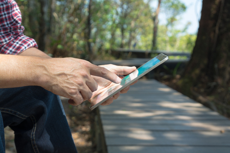 Male Hand use Digital Mobile Wireless Tablet PC to read e-mail or E-book and Travel information map while travel Trekking in forest National Park as Internet Technology for Trekker Hiker Telecommunication Concept.の写真素材