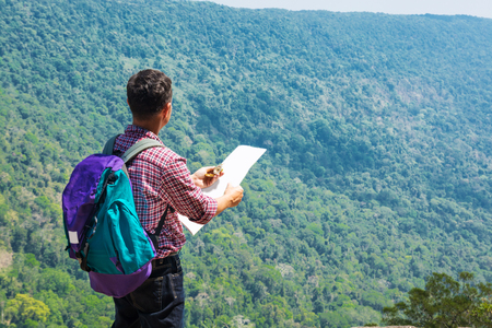 Male Backpacker Traveler or Trekker Stand on Cliff use Navigation map and Compass while Hiking on Green Nature Mountain as Traveling Equipment Conceptの写真素材