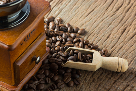Stack of Fresh Raw Coffee Beans on Wooden Desk Table with Wooden Spoon and Coffee Grinder as Refresh Beverages Conceptの写真素材