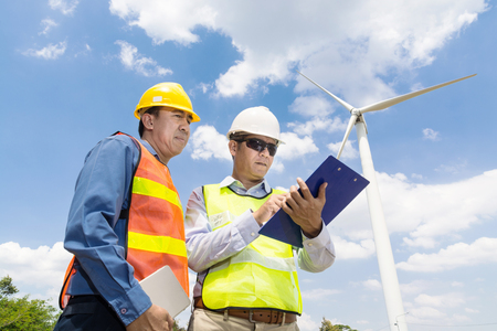 Alternative Power or Renewable Energy Technology Project Development Concept, Engineer and Architect discuss over Digital Wireless Tablet and Clipboard while working at Wind Turbine Power Generator Tower site.の写真素材