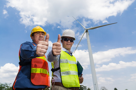 Male Architect and Engineer Smile and showing thumbs up together beside Wind Turbine power generator Site as Architecture Engineering Teamwork Attitude and Teamwork Concept.の写真素材