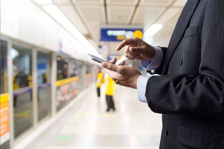 Hand of Businessman hold Wireless Digital Smart Device or Smartphone while waiting for Subway Train in Railway Stationの写真素材