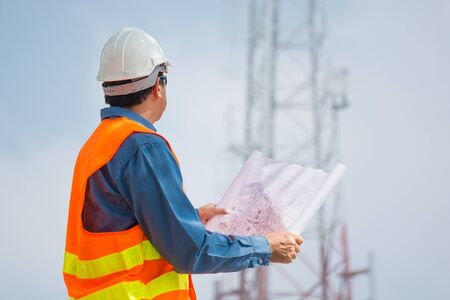 Engineer or Technocian hold plan and look at Telecommunication tower base Station or Network Cell...