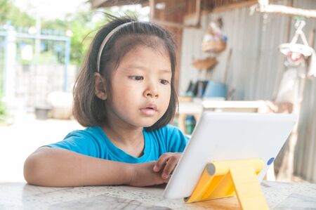 Asian Girl learning online course or playing game online on Digital Wireless Device or Tablet at...