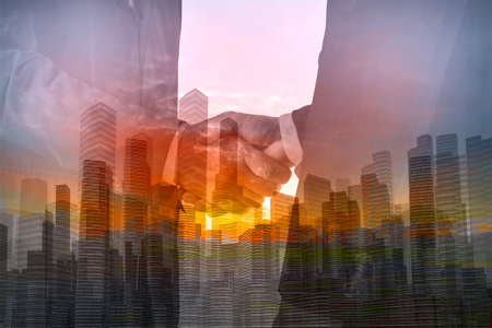 Double Exposure of Two Businessman shaking hand with City Building and Skyscraper as concept of Teamwork or Partnership business achievement.の写真素材