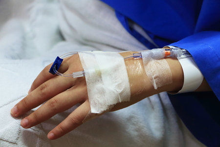 The woman patient in the hospital in blue dress in bed. Seeing the left hand was intravenous injection by dropping bottle.の写真素材