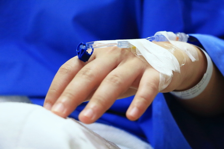 The woman patient in the hospital in blue dress in bed. Seeing the left hand was intravenous injection by dropping bottle.の写真素材