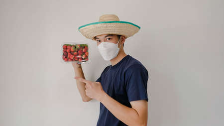 Man wearing a mask holding a box of strawberries. Please Mot. Strawberry fruit souvenirs.