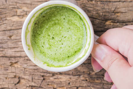 Hot green tea latte with matcha powder on wooden background.