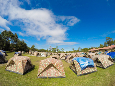 Camp tent stands in the meadow near the tree at autumn landscape background with mountains at the horizon under blue cloudy sky and light of rising sun.の写真素材