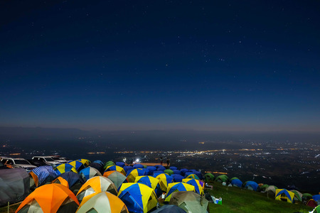 Night mountain landscape with illuminated tent. Silhouettes of snowy mountain peaks and edges night sky with many stars and milky way on background illuminated orange tent on foregroundの写真素材
