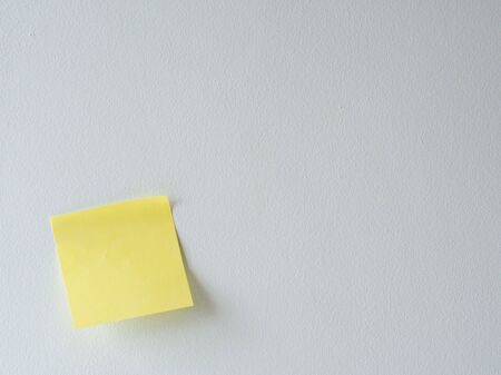 Blank yellow sticky note on a white wall. School and business concept.の写真素材