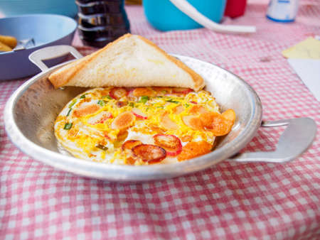 Closeup of fried eggs with sausages and chives in a small steel pan and a piece of buttered toast. Chiang Rai, Thailand. Travel and cuisine.の写真素材
