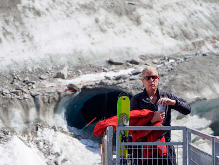 CHAMONIX, FRANCE - APRIL 26, 2018: A man with skis and a red jacket stops for a drink on the railings leading to an ice cave in the Mer de Glace glacier. Travel and nature.のeditorial素材