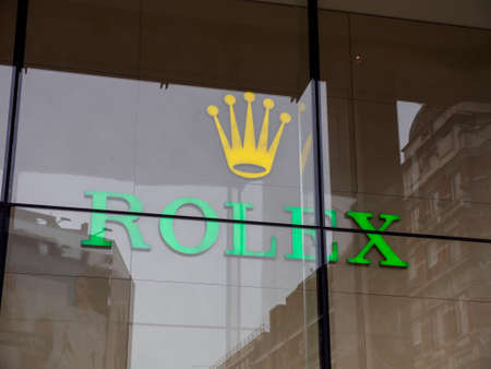 LONDON, ENGLAND - MARCH 8, 2019: Close-up detail of the Rolex logo and the iconic yellow crown behind a glass window at a Knightsbridge authorized dealer. Luxury timepieces and fashion.のeditorial素材