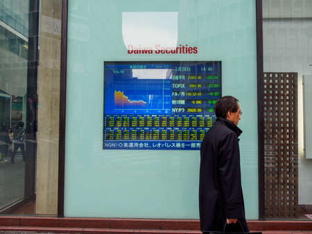 TOKYO, JAPAN - MARCH 28, 2019: A salaryman walks pass a screen displaying TOPIX stock index prices...