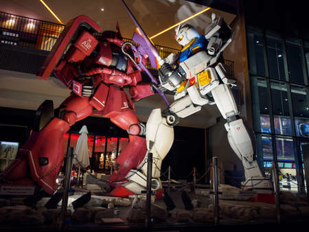OSAKA, JAPAN - APRIL 3, 2018: Wide closeup of the Gundam and Zaku life-sized mecha replicas posed in battle in front of EXPOCITY Shopping mall at night. Travel and Anime tourism.のeditorial素材