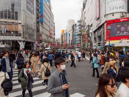 TOKYO, JAPAN - MARCH 28, 2019: Wide angle view of waves of pedestrians walking the famed and busy Shibuya Crossing from the shopping street on a cloudy afternoon. Travel and tourism.のeditorial素材