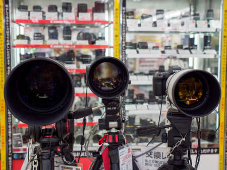 OSAKA, JAPAN - APRIL 3, 2018: Closeup detail of multiple Canon and Nikon DSLR cameras with large telephoto lens and tripods on sale at a Bic Camera. Dotonbori, Namba. Travel and electronics business.のeditorial素材