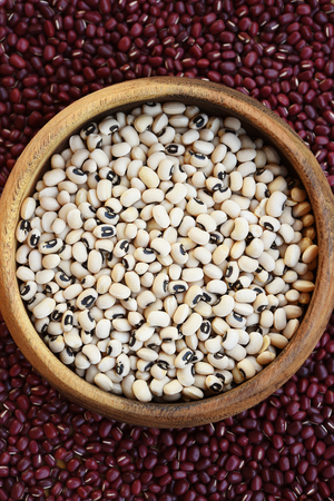 Black eyed peas in wooden bowl on red bean backgroundの写真素材