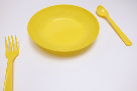 Set of a yellow plate, spoon and fork isolated on white backgroundの写真素材