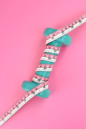 Fitness concept dumbbell and measuring tape on pink backgroundの写真素材