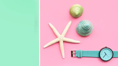 close up of seashell and starfish with wrist watches on pink and green background