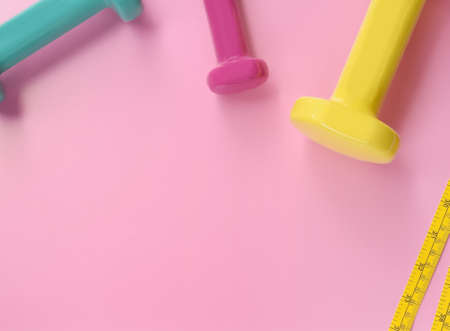 Fitness concept dumbbell and measuring tape on pink background