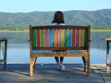 Woman sitting on a bench at a water and mountainsの写真素材