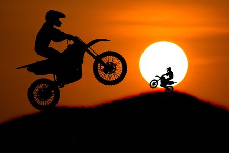 silhouette of Motorbike rider jump cross slope of mountain with sunset backgroundの写真素材
