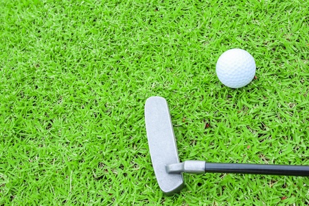 golf ball on a tee and putter in green grass course