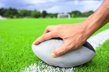 rugby ball in hand on green grass の写真素材