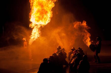 Silhouette of Firemen fighting a raging fire with huge flames of burning timberの写真素材