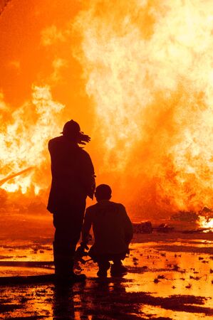 Silhouette of Firemen fighting a raging fire with huge flames of burning timberの写真素材