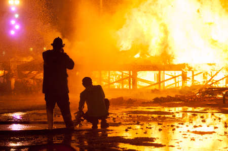 Silhouette of Firemen fighting a raging fire with huge flames of burning timber
