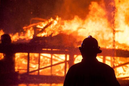 Silhouette of Firemen fighting a raging fire with huge flames of burning timberの写真素材