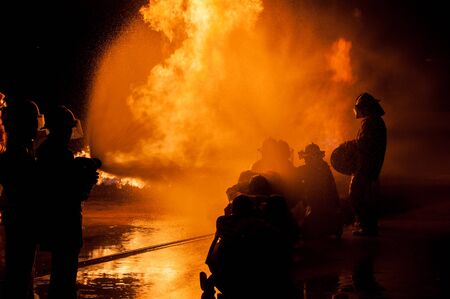 Silhouette of Firemen fighting a raging fire with huge flames of burning timberの写真素材