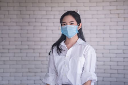 beautiful young asian woman wearing face mask to protect covid19 virus against white brick wallの写真素材