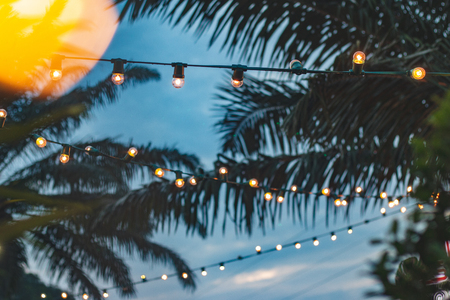 blurred light bokeh with coconut palm tree background on sunset, yellow string lights with bokeh decor in outdoor restaurantの写真素材