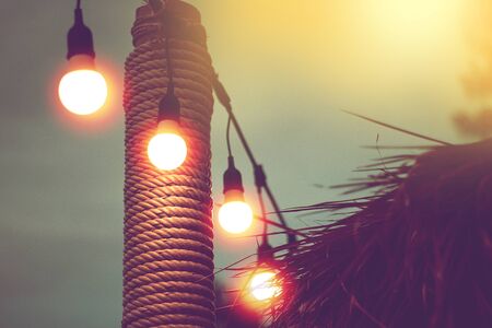blurred light on sunset with yellow string lights decor in beach restaurantの写真素材