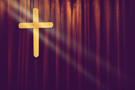yellow wood cross on dark brown curtain background in small church with ray of lightの写真素材