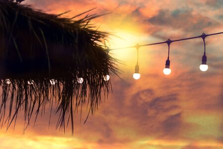blurred bokeh light on sunset with yellow string lights decor in beach restaurantの写真素材